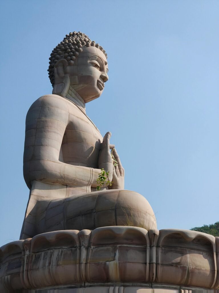 A serene side view of a large Buddha statue against a clear blue sky.